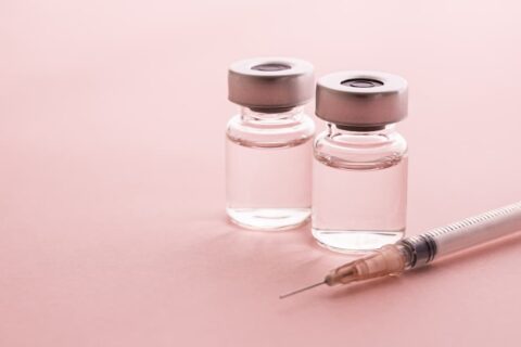 Two glass vials of clear injectable liquid and a medical syringe on a pink background, illustrating the differences between Botox, Dysport, and Xeomin treatments.